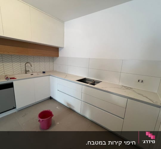 מטבח בשיפוץ עם ארונות לבנים ודלי על הרצפה